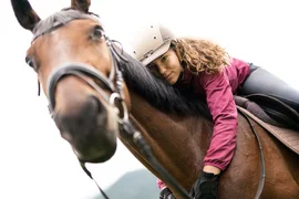 First happiness of riding / 3 nights Woman wearing helmet hugging horse closely, horse's nose in foreground