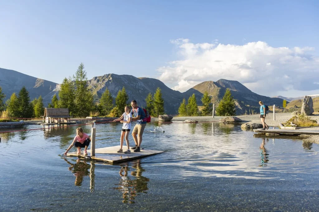 Family fishing on wooden platform in mountain lake under clear sky