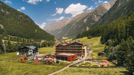 Blick auf ein Dorf mit Spielplatz in einem grünen Tal zwischen bewaldeten Bergen