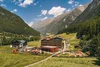 Blick auf ein Dorf mit Spielplatz in einem grünen Tal zwischen bewaldeten Bergen