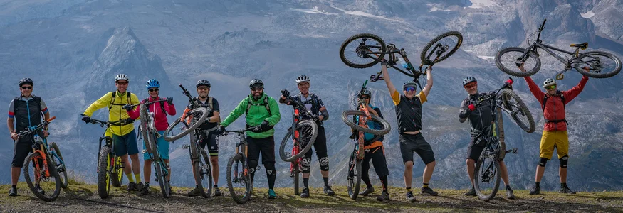 Neun Radfahrer mit Mountainbikes auf Bergpfad vor schneebedeckten Gipfeln
