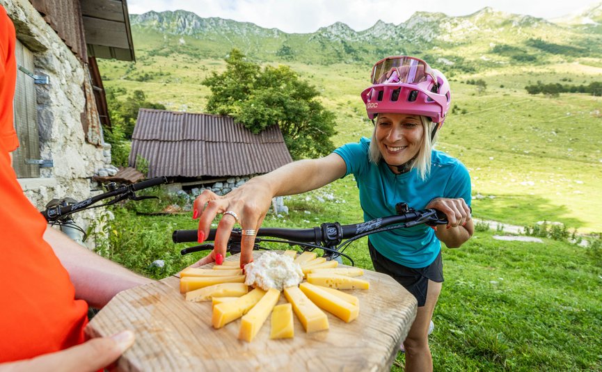 Woman in bike helmet reaching for cheese on wooden board in mountains