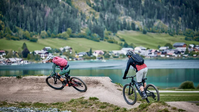 Twee fietsers op een mountainbiketraject met meer en bergen op de achtergrond