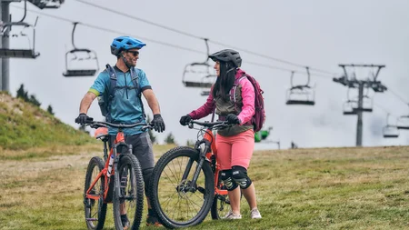 Zwei Mountainbiker mit Helmen und Schutzkleidung stehen mit Fahrrädern auf einer Wiese