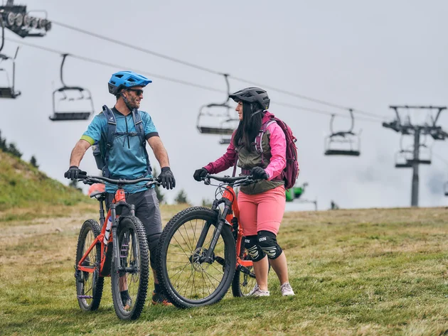 Zwei Mountainbiker mit Helmen und Schutzkleidung stehen mit Fahrrädern auf einer Wiese