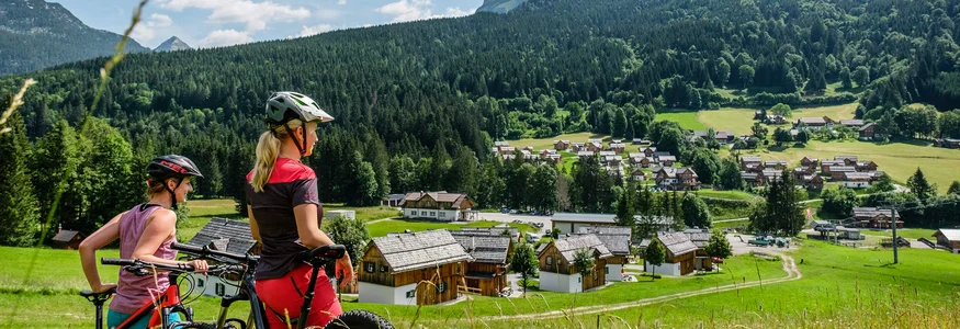 Twee fietsers kijken uit over een dorp in een groen berglandschap