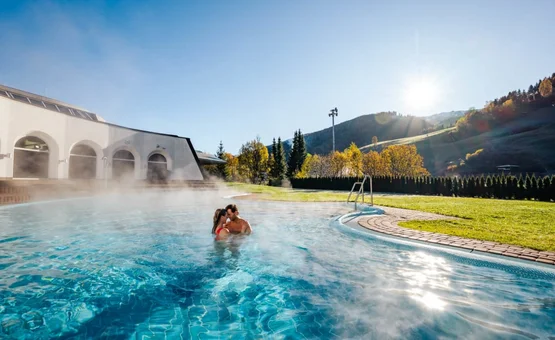 Couple relaxing in heated outdoor pool with mountain view on sunny day