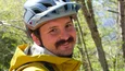 Mann in gelber Jacke und Helm steht neben einer Reihe von Mountainbikes im Wald