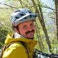 Man in gele jas en helm staat naast een rij mountainbikes in het bos
