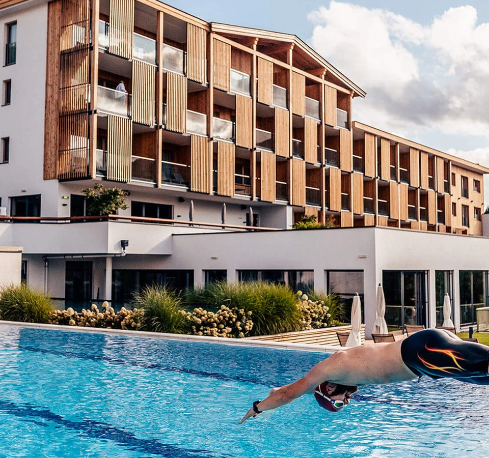 Mann taucht in einen Außenpool vor einem modernen Hotelgebäude ein