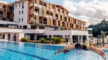 Mann taucht in einen Außenpool vor einem modernen Hotelgebäude ein