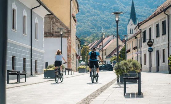 Two people cycling down a quiet town street with mountains in the background