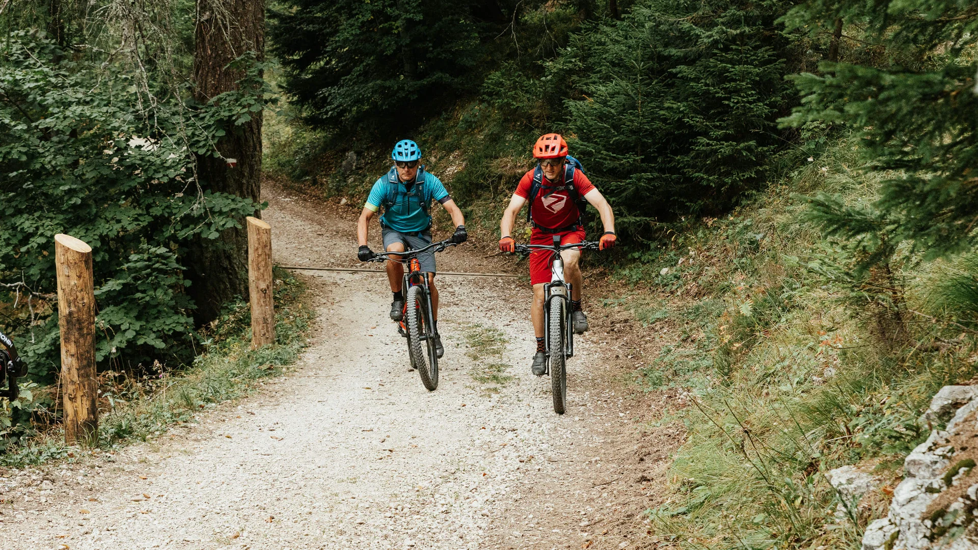 Zwei Mountainbiker fahren auf einem Waldweg unter einer Stange durch