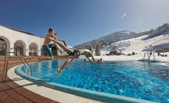 Twee jongens springen in een buitenzwembad met besneeuwde bergen op de achtergrond