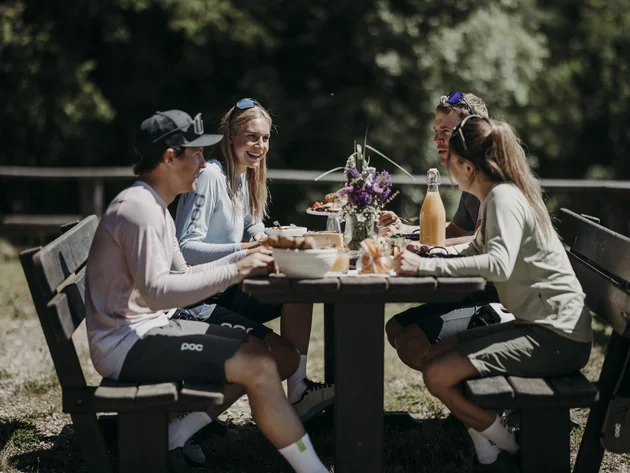 Was steckt hinter dem Umweltengagement von Bikehotels? Vier junge Menschen sitzen draußen am Tisch und essen gemeinsam
