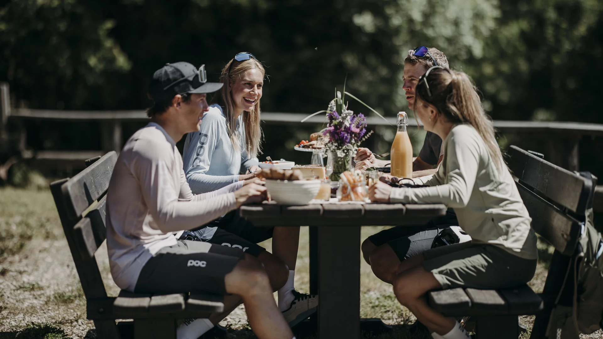 Vier junge Menschen sitzen draußen am Tisch und essen gemeinsam
