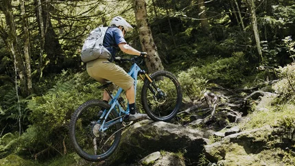 Mountainbiker mit Helm und Rucksack fährt über einen felsigen Waldweg