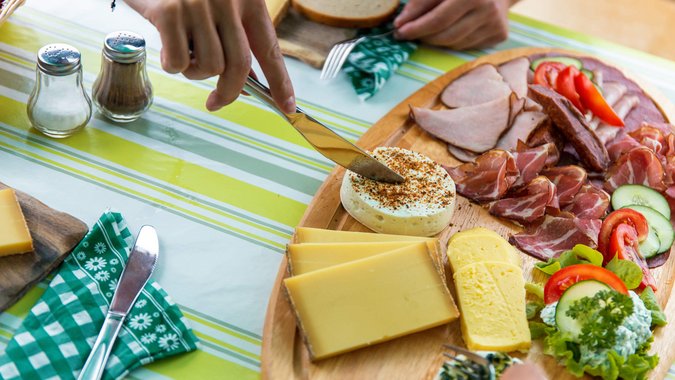 Messer schneidet Käse auf einer Platte mit verschiedenen Käsesorten und Wurst