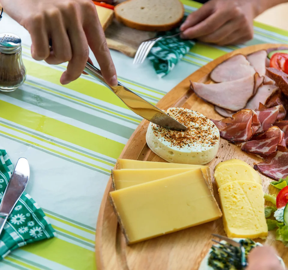 Messer schneidet Käse auf einer Platte mit verschiedenen Käsesorten und Wurst