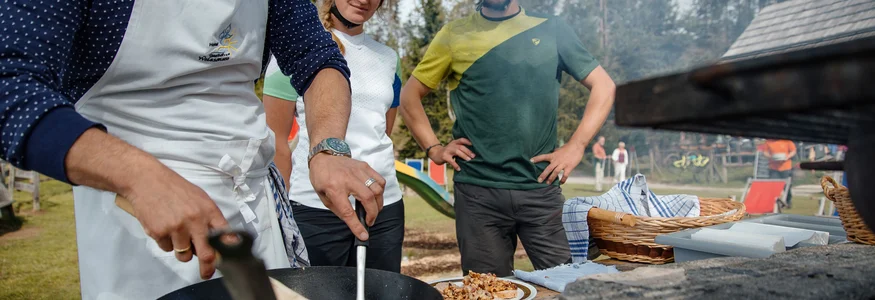 Mann kocht im Freien, zwei Radfahrer beobachten ihn