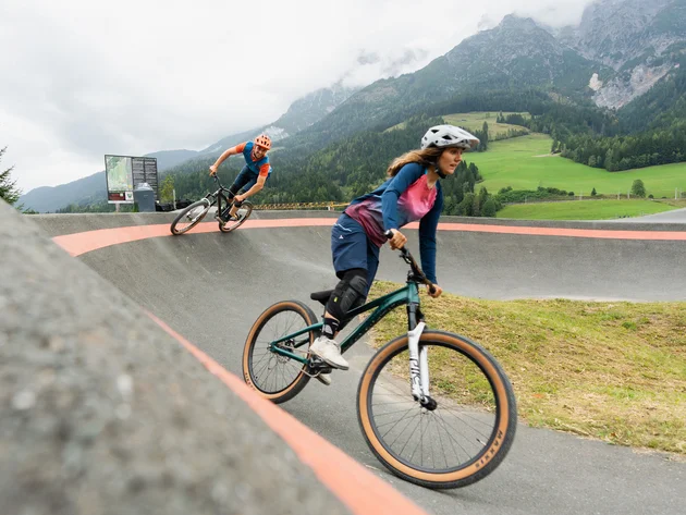 Happy Birthday EPIC Bike Park! © Patrick Wasshuber Frau und Mann fahren Mountainbike auf einer geschwungenen Strecke in den Bergen