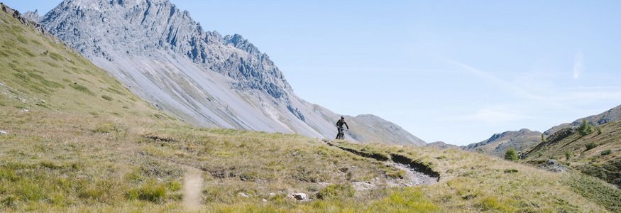 Mountainbiker fährt auf einem Pfad durch eine Bergwiese unter klarem Himmel