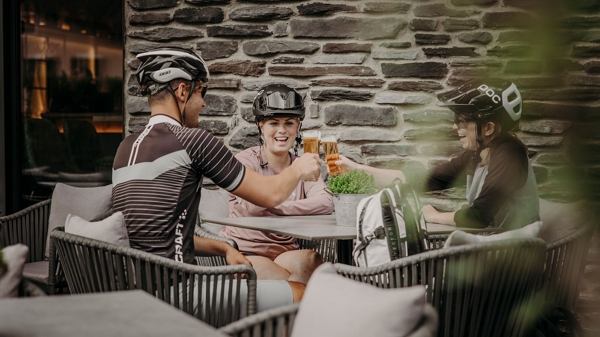 Drei Radfahrer mit Helmen stoßen mit Getränken an in einem Café