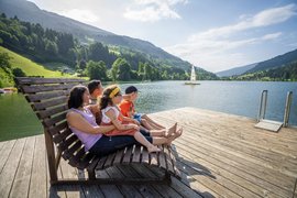 Family sitting on a dock looking at a lake and sailboats in the mountains