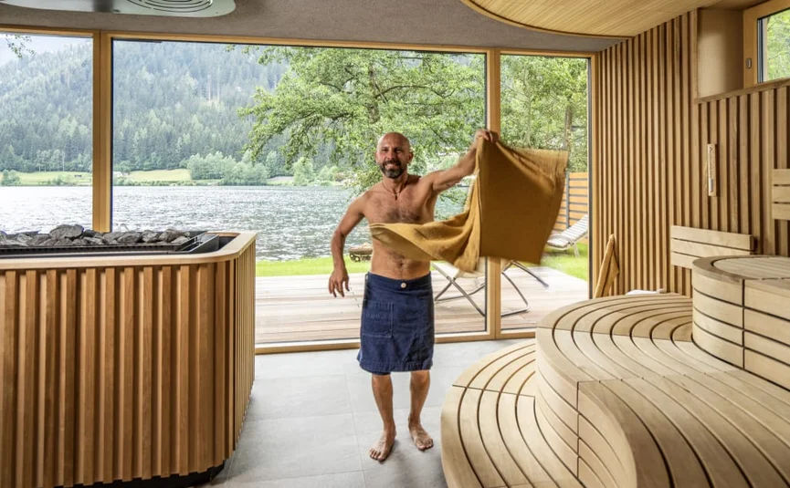 Man with towels in modern sauna with lake and mountain view