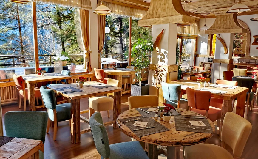 Helles Restaurant mit Holztischen und bunten Stühlen mit Blick auf den Wald