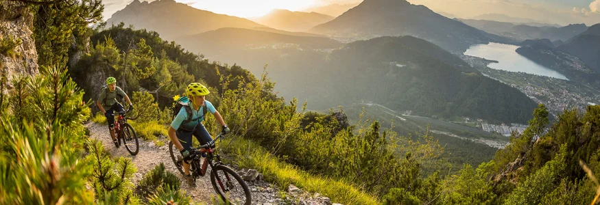 Two mountain bikers riding on a mountain trail at sunset with lake view