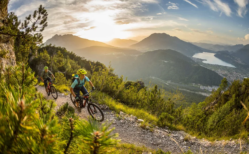 Two mountain bikers riding on a mountain trail at sunset with lake view