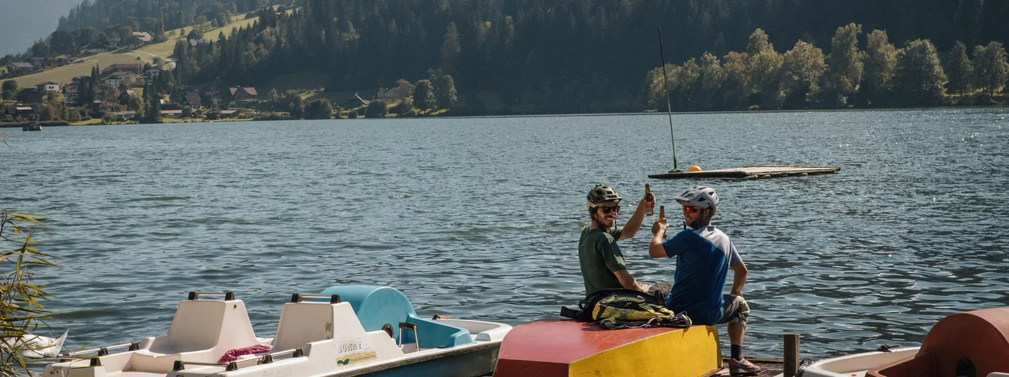Twee fietsers op steiger aan meer met bergen op achtergrond proosten
