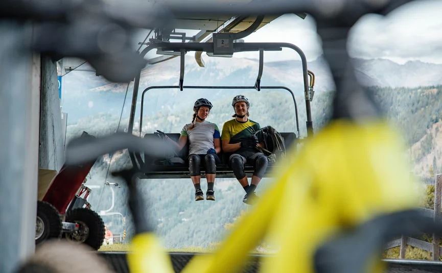 Zwei Radfahrer auf Sessellift mit Blick auf Berge