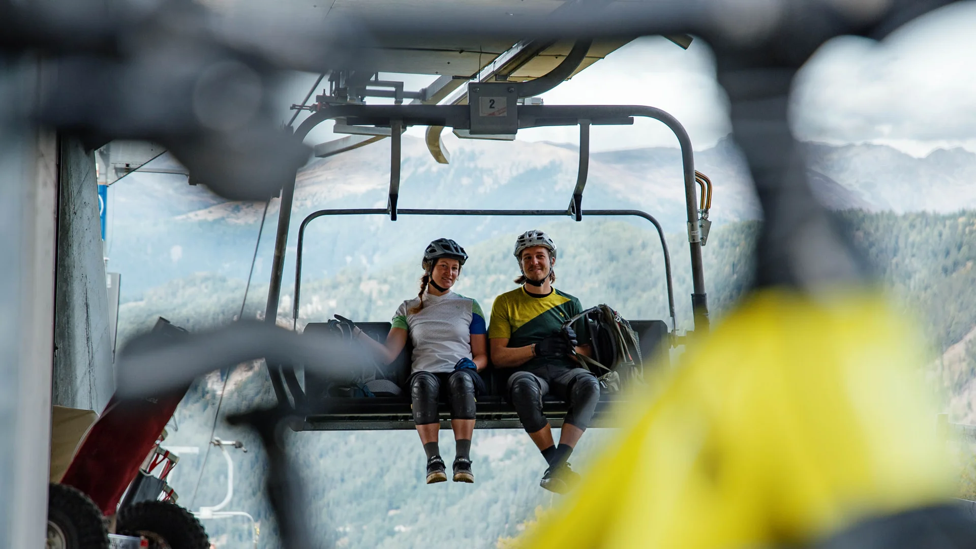 Zwei Radfahrer auf Sessellift mit Blick auf Berge
