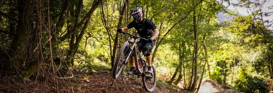 Mountainbiker springt im Wald auf einem Trail über eine Erhebung