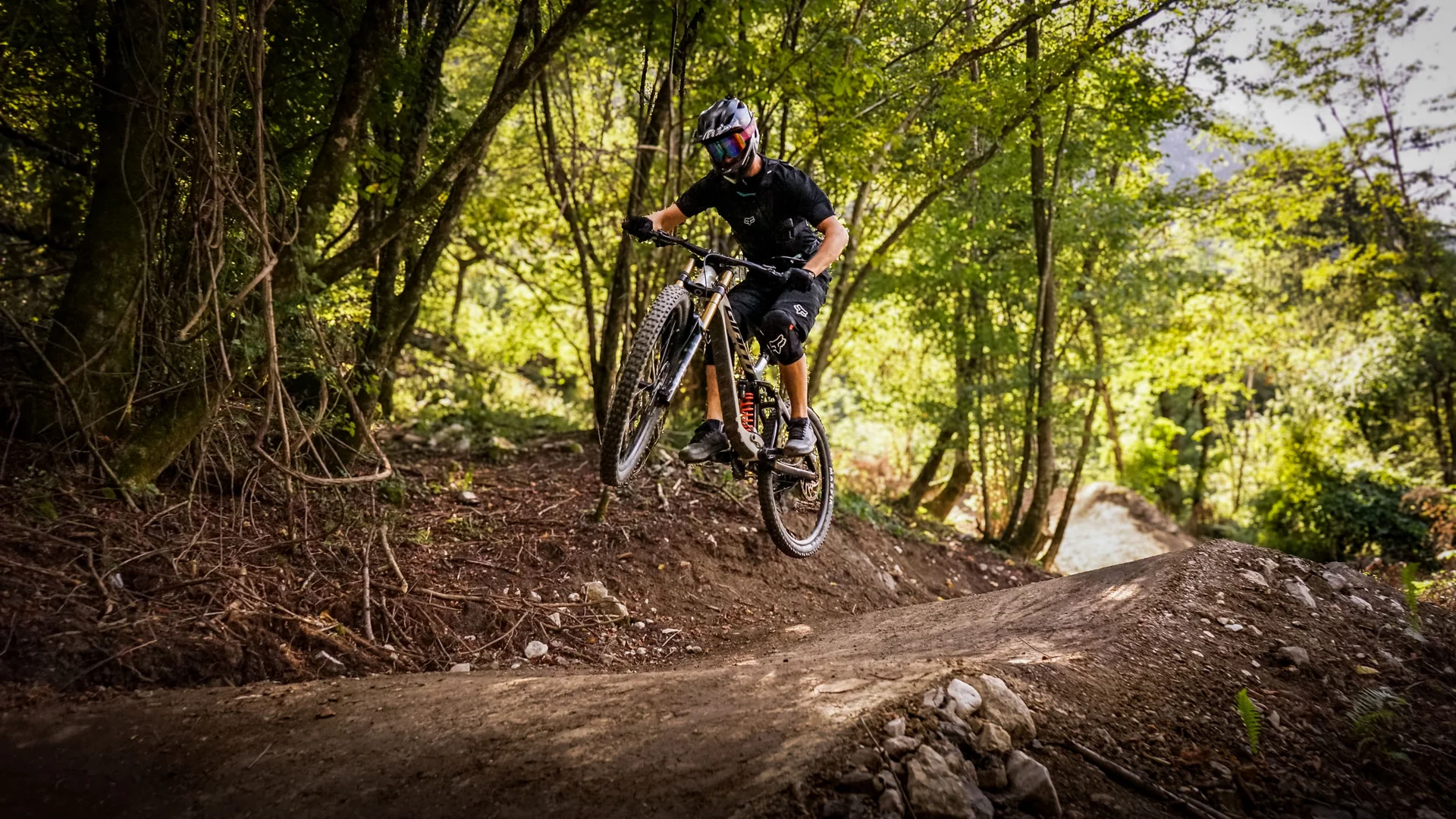 Dein Julische Alpen-Guide © Bike Park Bovec Mountainbiker springt im Wald auf einem Trail über eine Erhebung