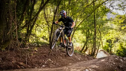 Mountainbiker springt im Wald auf einem Trail über eine Erhebung