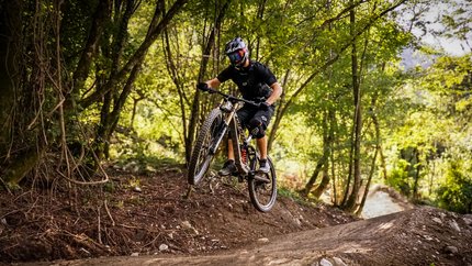 Airline © Bike Park Bovec Mountainbiker springt im Wald auf einem Trail über eine Erhebung