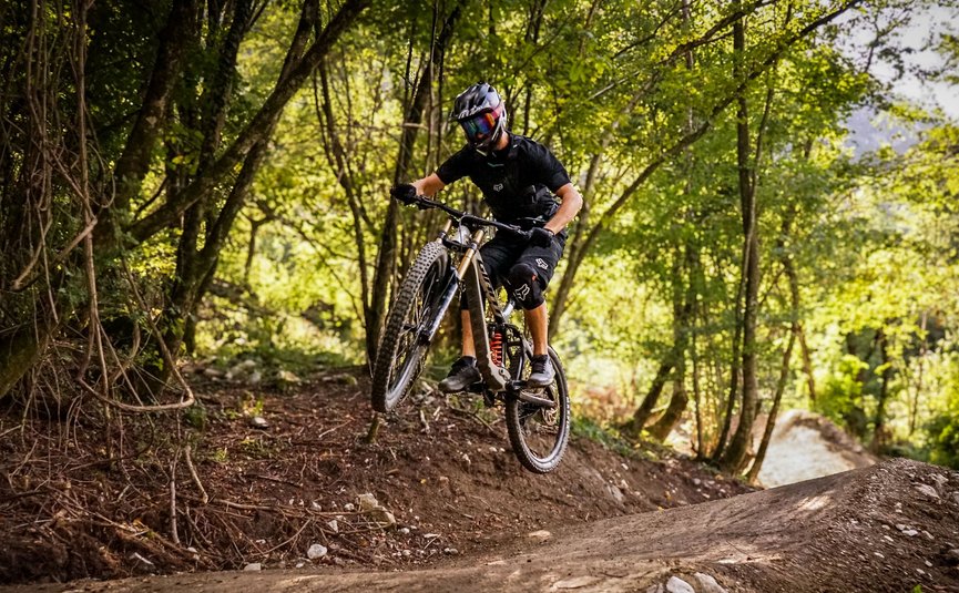 Airline © Bike Park Bovec Mountainbiker springt im Wald auf einem Trail über eine Erhebung