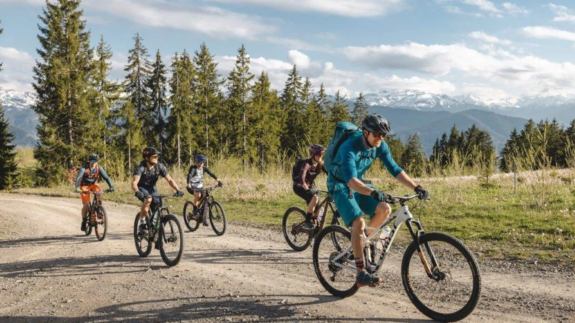 Fünf Fahrradfahrer fahren auf einem Waldweg mit Bergen im Hintergrund