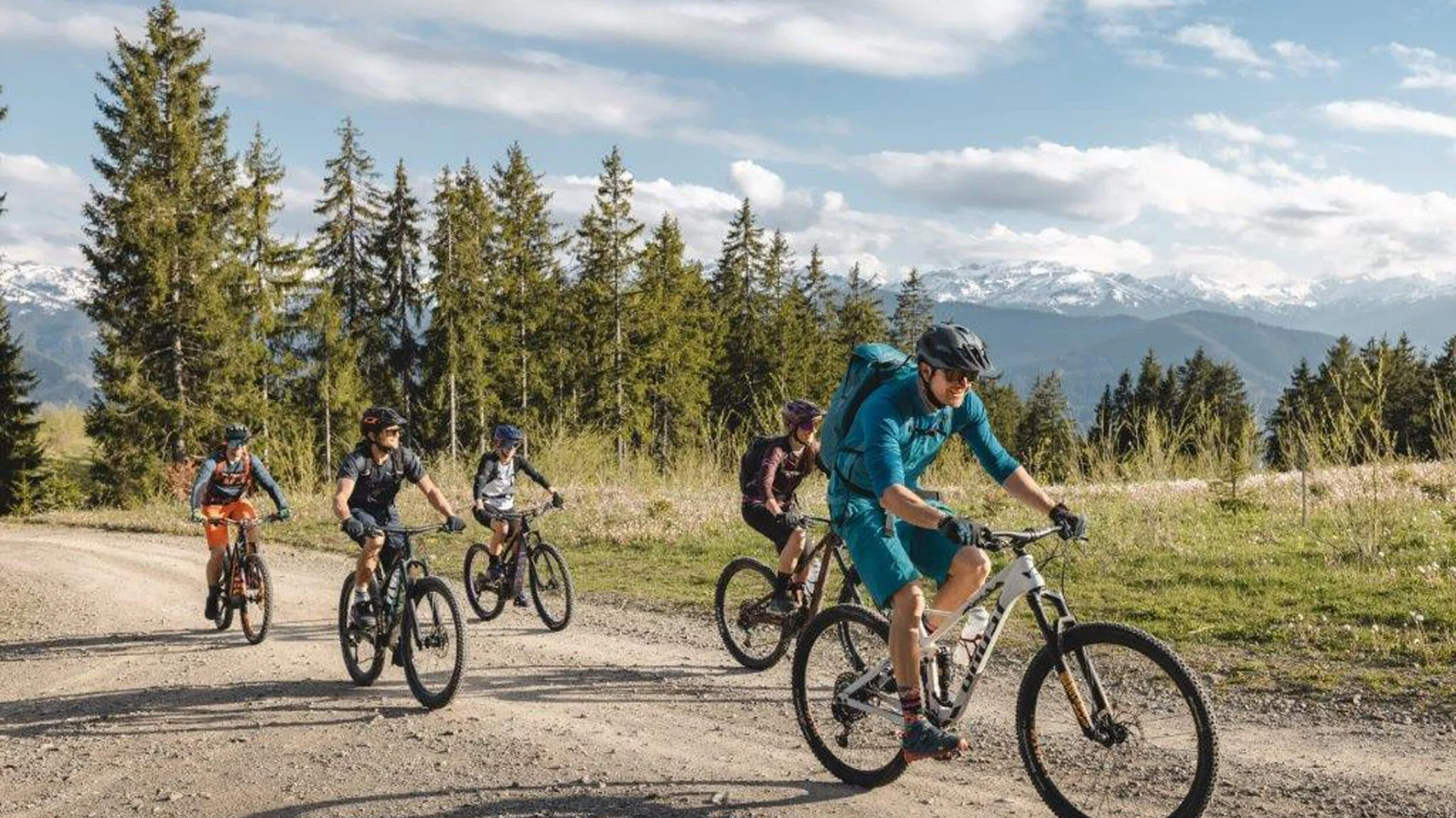 Fünf Fahrradfahrer fahren auf einem Waldweg mit Bergen im Hintergrund