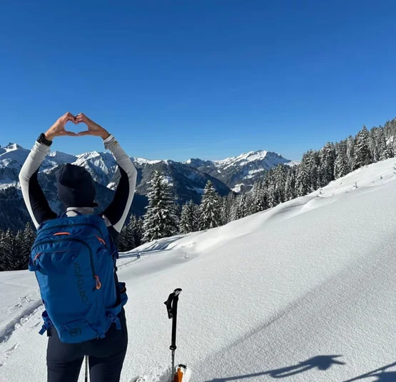 Winter Special Wanderer formt mit den Händen ein Herz vor verschneiten Bergen