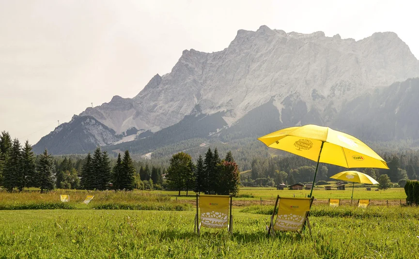 Gelbe Stühle und Sonnenschirme auf einer Wiese vor Bergkulisse