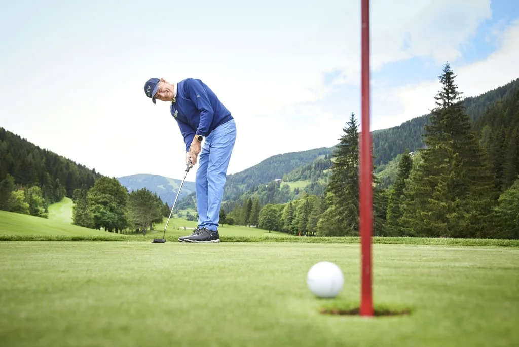 Man playing golf on green course with mountains in the background