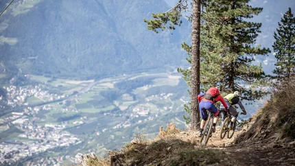 Zwei Mountainbiker fahren auf einem Bergpfad mit Talblick