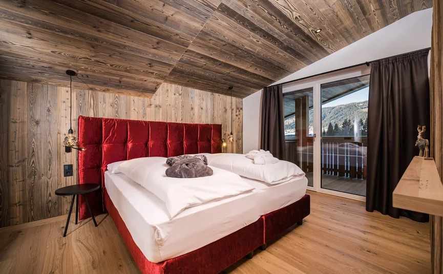 Gezellige slaapkamer met rood bed en houten muren met uitzicht op bergen
