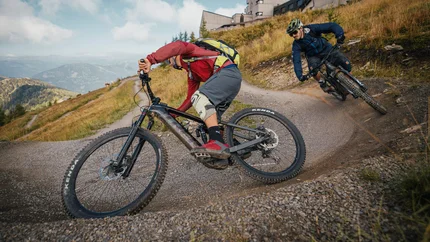 Twee mountainbikers rijden een kronkelig grindpad bergaf