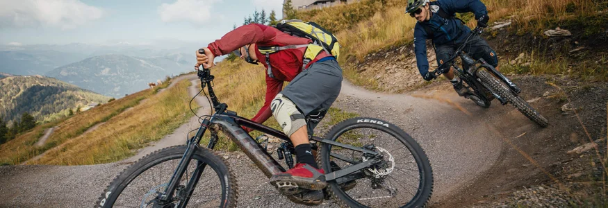 Zwei Mountainbiker fahren eine kurvige Schotterpiste in den Bergen hinunter