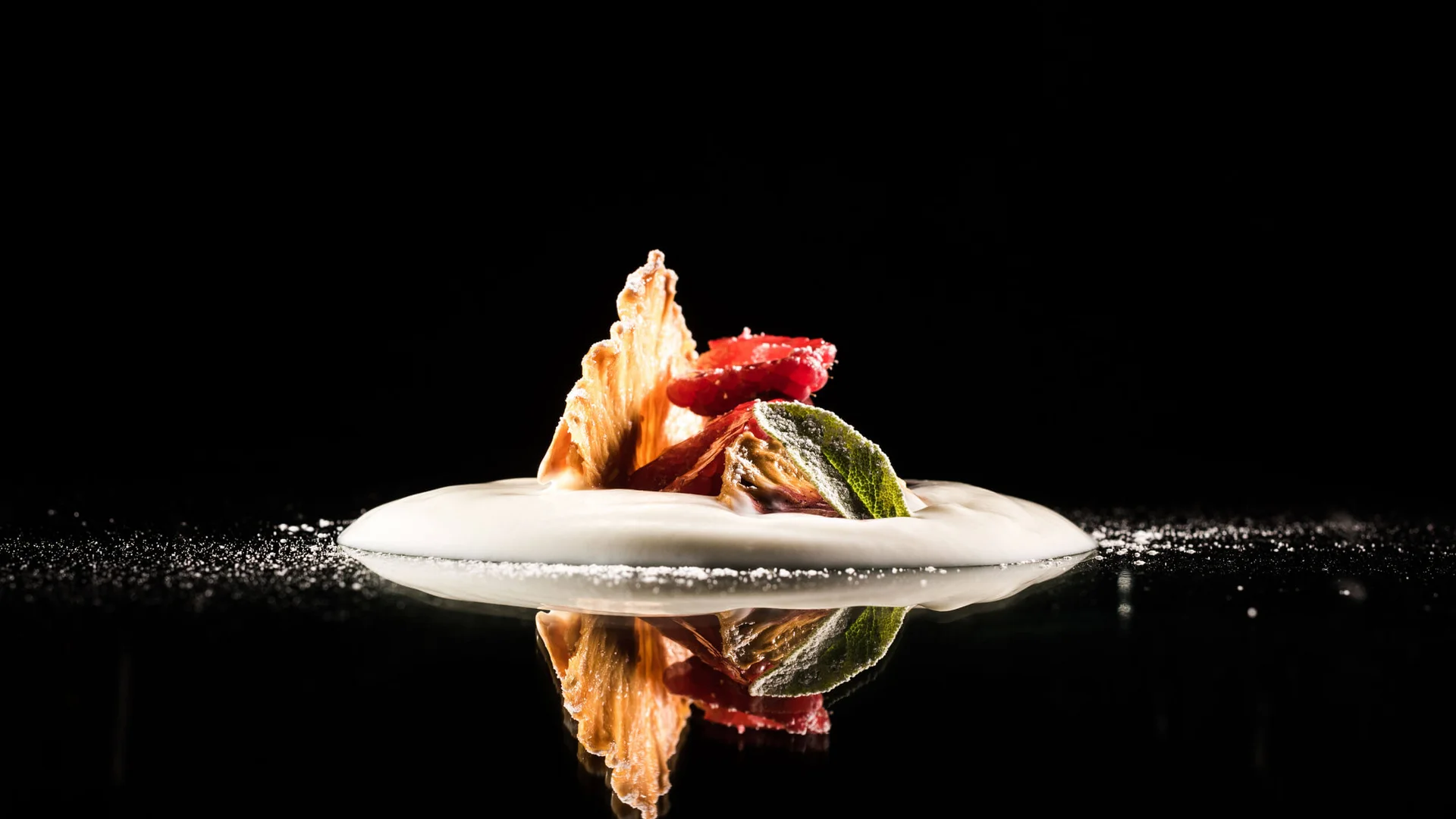 Kreativ angerichtetes Dessert mit Schaum und Fruchtscheiben auf schwarzem Hintergrund